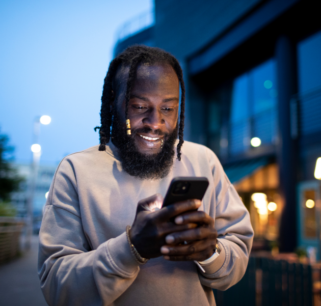 Man smiling while using a smartphone outdoors in the evening
